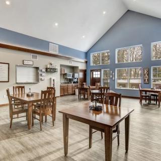 A modern dining area with wooden tables and chairs, featuring a vaulted ceiling and large windows that let in natural light.