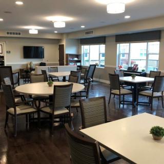 A community dining area with several tables and chairs, featuring wooden floors and large windows.