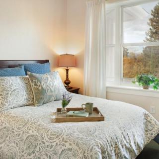 A cozy bedroom with elegant bedding, a bedside lamp, and a window offering a scenic view.