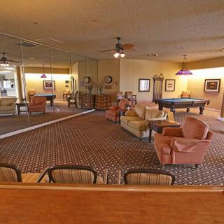 A cozy lounge with a seating area and a pool table, featuring carpeted flooring and ceiling fans.