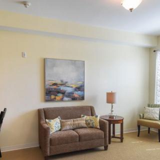 A cozy living room featuring a sofa with cushions, a side table with a lamp, and a painting on the wall.