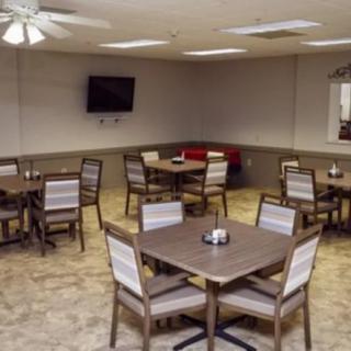 An empty dining room with multiple tables and chairs, a television on the wall, and a ceiling fan overhead.