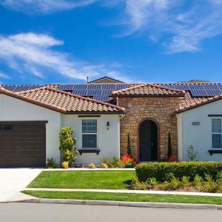 A modern house with solar panels on the roof, a well-maintained garden, and a driveway.