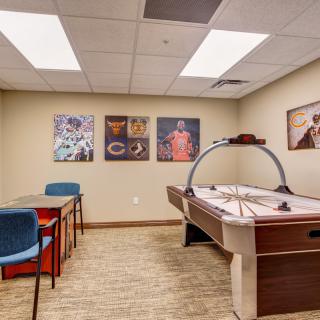 A game room featuring an air hockey table, a small table with chairs, and colorful posters on the walls.