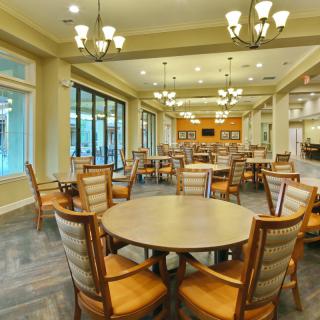 A spacious dining area with round tables and comfortable chairs, well-lit by elegant chandeliers.