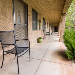 A view of a motel corridor with metal chairs and potted plants along the walkway.
