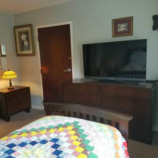 A cozy bedroom with a colorful quilt, large TV, and warm lighting.