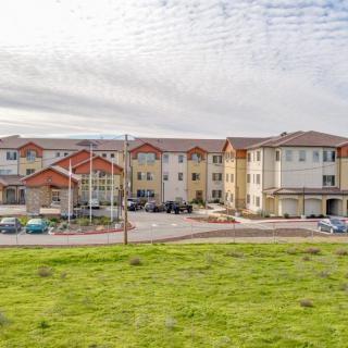 A modern apartment complex with a spacious parking lot, set against a cloudy sky.