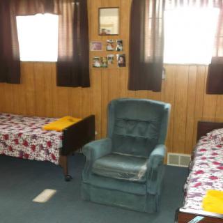 A cozy bedroom with two twin beds, an armchair, and wood-paneled walls.