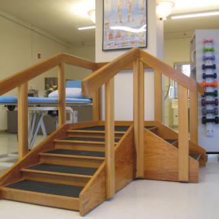 A wooden staircase designed for rehabilitation and therapy, featuring handrails and non-slip surfaces.