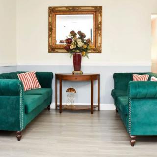 A cozy living room with matching green sofas, a wooden table, and a decorative mirror.