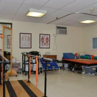 A physical therapy room equipped with parallel bars, exercise mats, and medical posters.