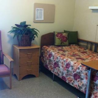 A cozy bedroom featuring a single bed with floral bedding, accompanied by a wooden cabinet and a chair, creating a warm and inviting atmosphere.