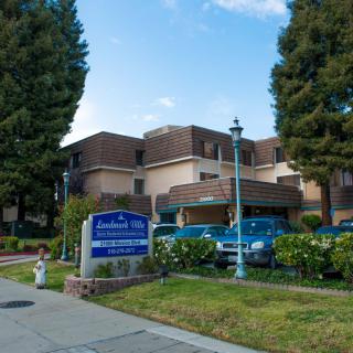 A residential building with a sign and parked cars, surrounded by trees under a cloudy sky.