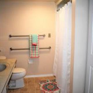 A cozy bathroom with towels on the wall, a white shower curtain, and a colorful rug.