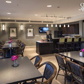 A modern dining area with tables, chairs, and a bar equipped with stools, featuring contemporary lighting and decor.