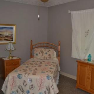 A cozy bedroom with a single bed and wooden furniture, decorated with a floral bedspread and a painting on the wall.