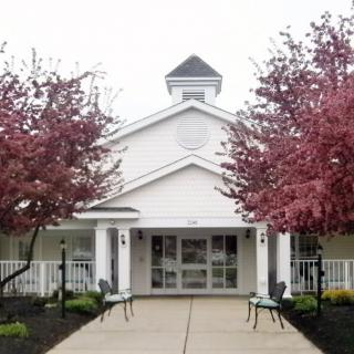 A white building with a central entrance, flanked by trees with pink blossoms.