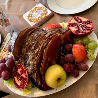 A vibrant platter featuring a beautifully roasted meat centerpiece surrounded by an assortment of fresh fruits.
