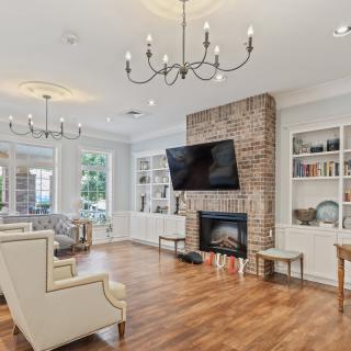 A stylish living room featuring a brick fireplace with a mounted TV, elegant chandeliers, and built-in bookshelves.