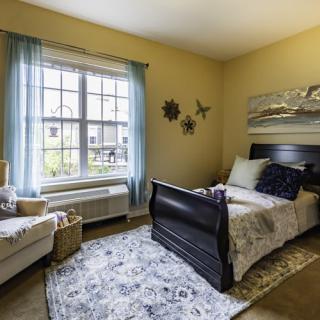A cozy bedroom with a single bed, armchair, and large window.