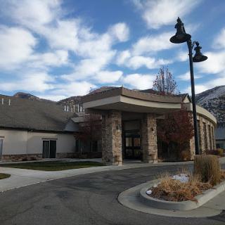 A modern building with a curved entrance, surrounded by landscaped areas and under a cloudy sky.