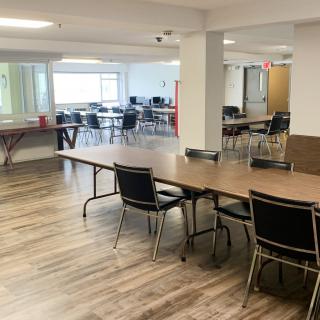 A spacious meeting room with several tables and chairs, featuring large windows providing natural light.