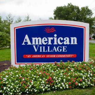 Community entrance sign for American Village surrounded by landscaped flowers.