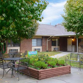 A serene outdoor space featuring a garden, seating area, and a residential building in the background.