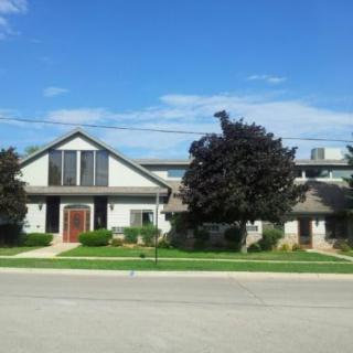 A suburban house with a well-maintained lawn and trees under a clear blue sky.