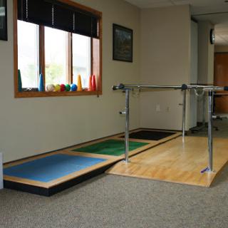 A well-lit rehabilitation space featuring exercise equipment including a barre and colorful mats.