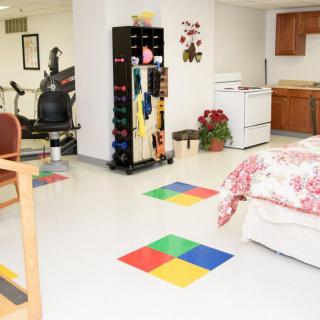 A multipurpose living space with gym equipment, a small kitchen area, and colorful floor tiles.