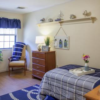 A cozy bedroom with a single bed, dresser, and window with blue curtains.