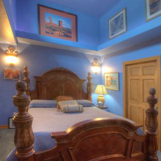 A cozy bedroom with blue walls and a wooden bed, adorned with lamps and artwork.
