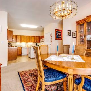 A cozy dining area with a wooden table and chairs, accented by a chandelier, adjacent to an open kitchen.