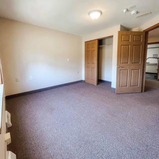 An empty carpeted room with a closet and open door.
