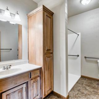 A modern bathroom featuring a wooden vanity with a sink and mirror, adjacent to a shower with a handrail.