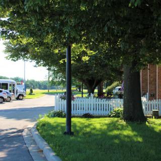 A suburban street with a van parked near a house, surrounded by trees and a white fence.