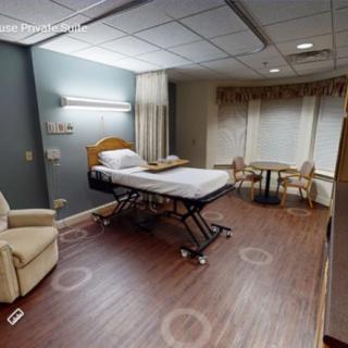 A hospital room with a patient bed, seating area, and large windows.