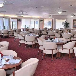 An empty indoor dining area with neatly arranged tables and chairs on a red carpet.