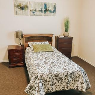 A neatly arranged bedroom with a single bed, flanked by two wooden nightstands and simple wall decor.