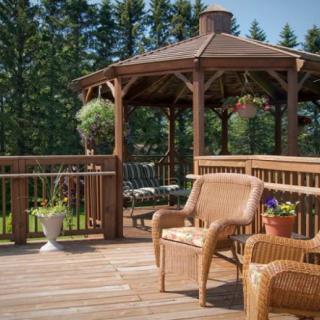 A sunny deck with wicker furniture and a wooden gazebo in a lush garden setting.