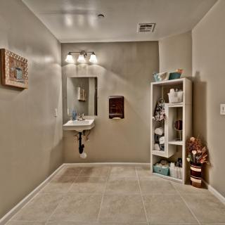 A tidy bathroom with a wall-mounted sink, mirror, and neatly organized shelving unit.