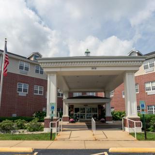 The entrance of a brick building with a covered walkway and an American flag nearby.