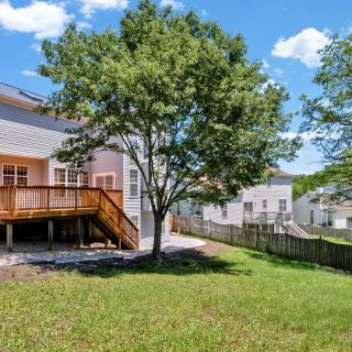 A suburban backyard with a deck, tree, and grassy area on a sunny day.