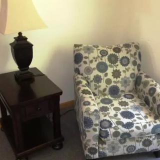 A cozy corner featuring a patterned armchair next to a dark wooden side table with a lamp.