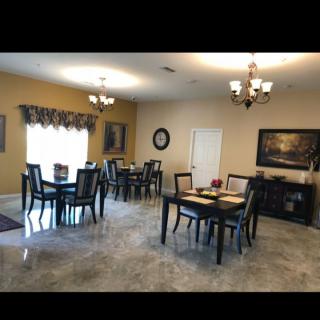 A spacious dining room with multiple tables and chairs, decorated with chandeliers and wall art.