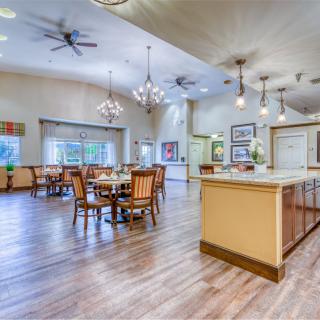 A spacious, modern dining area with wood flooring, elegant chandeliers, and ceiling fans, featuring tables and chairs arranged for comfort.