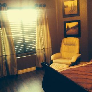 A cozy bedroom with a comfortable chair by the window, featuring elegant curtains and framed artwork.
