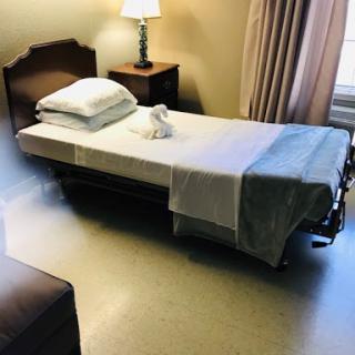 A clean and simple hospital room featuring a single bed, lamp, and nightstand.